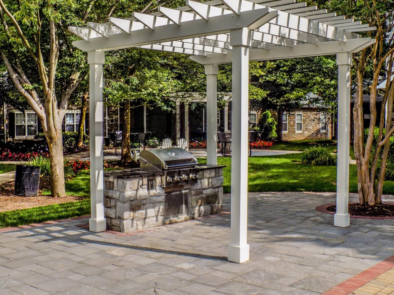 Stone grill island with built-in gas grill under a white pergola, built by Outdoor Solutions