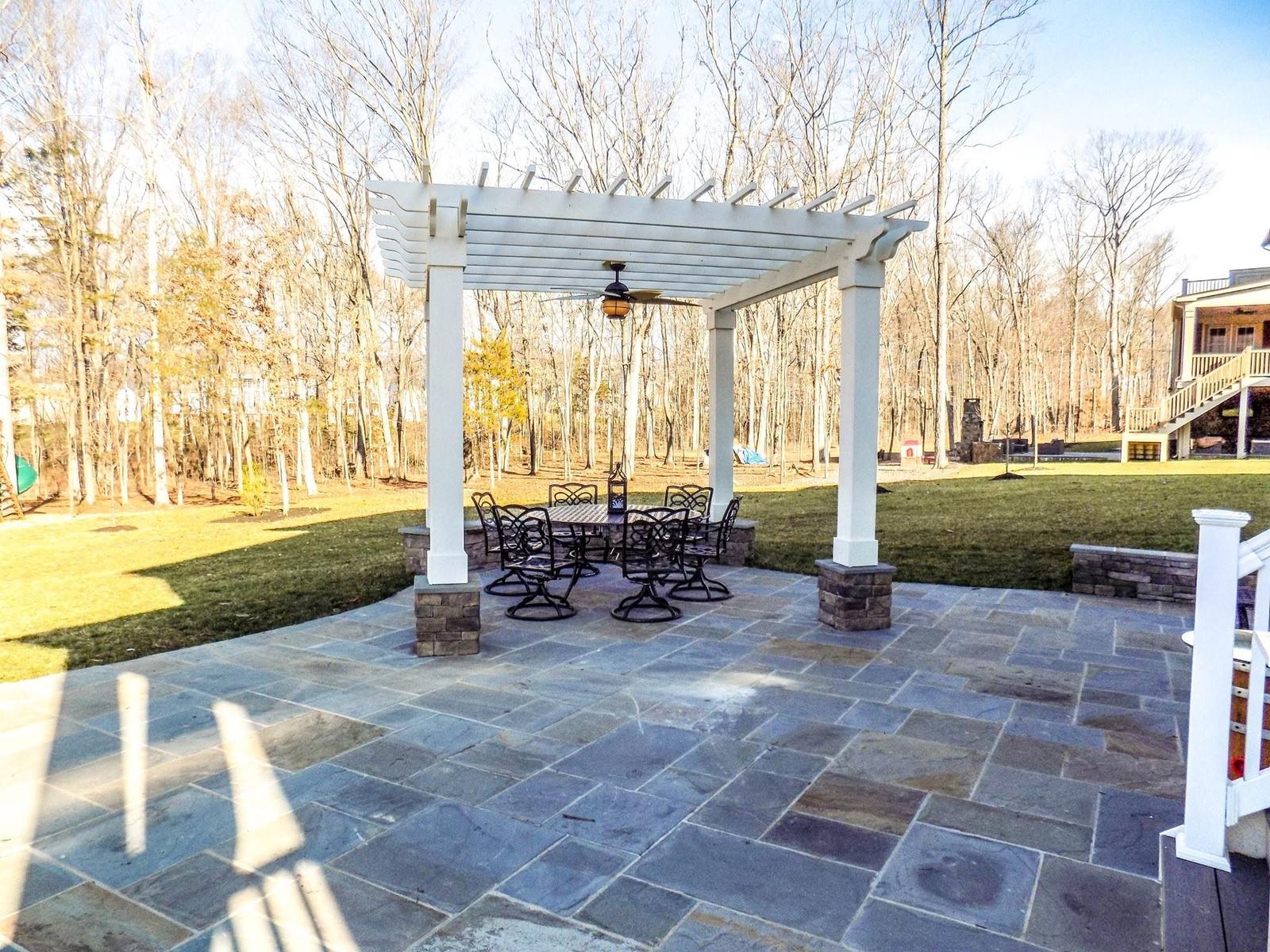White pergola with ceiling fan over a bluestone dining patio and sitting wall, built by Outdoor Solutions in Northern Virginia