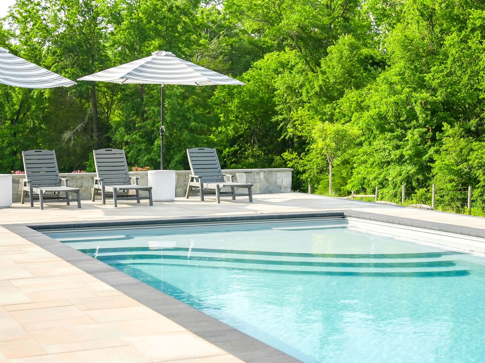 Fiberglass pool with tanning ledge, paver pool deck, and stone seating wall by Outdoor Solutions in Northern Virginia