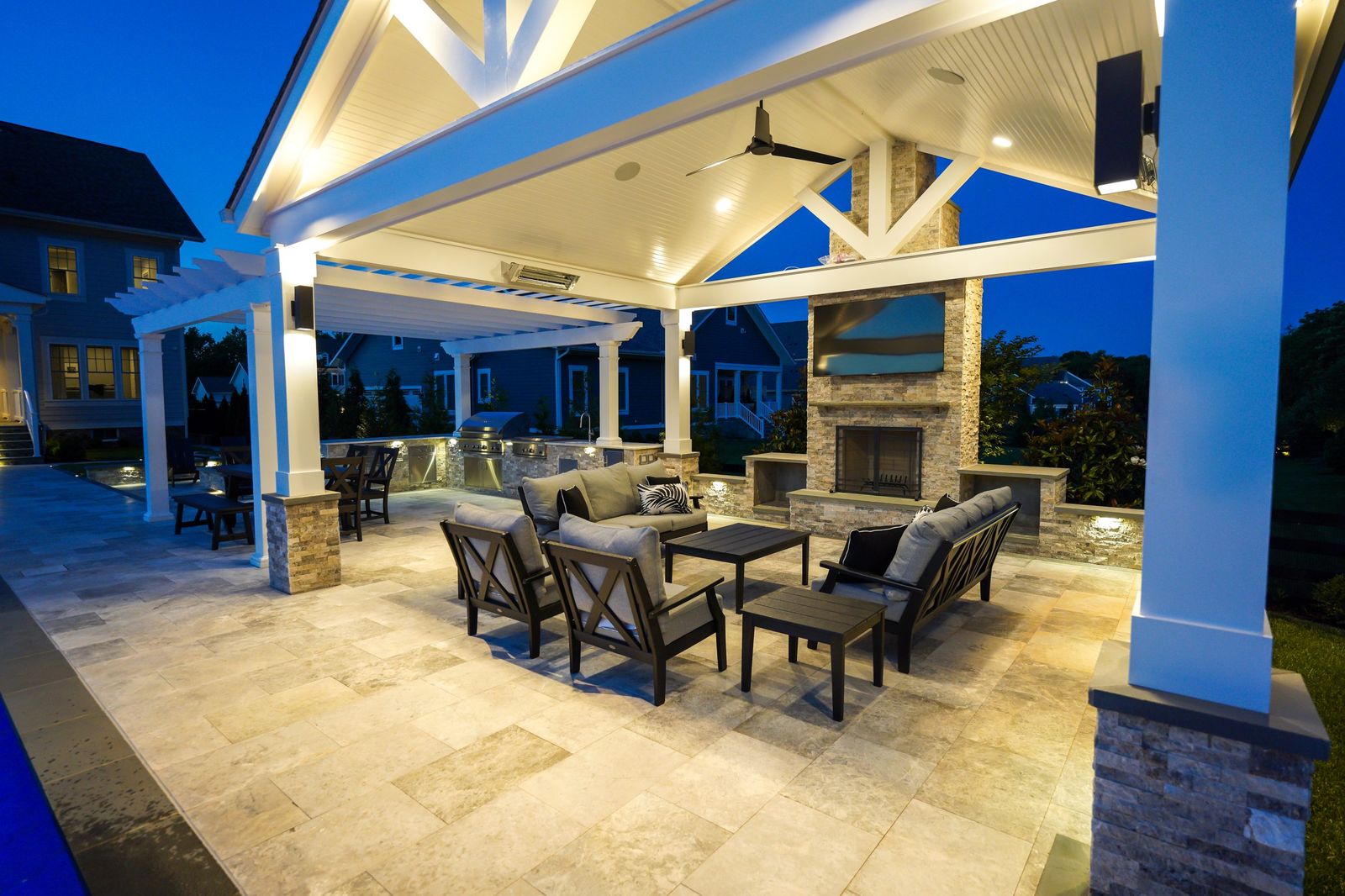 Covered outdoor living pavilion with stone fireplace and outdoor kitchen beside a pool, built by Outdoor Solutions in Northern Virginia