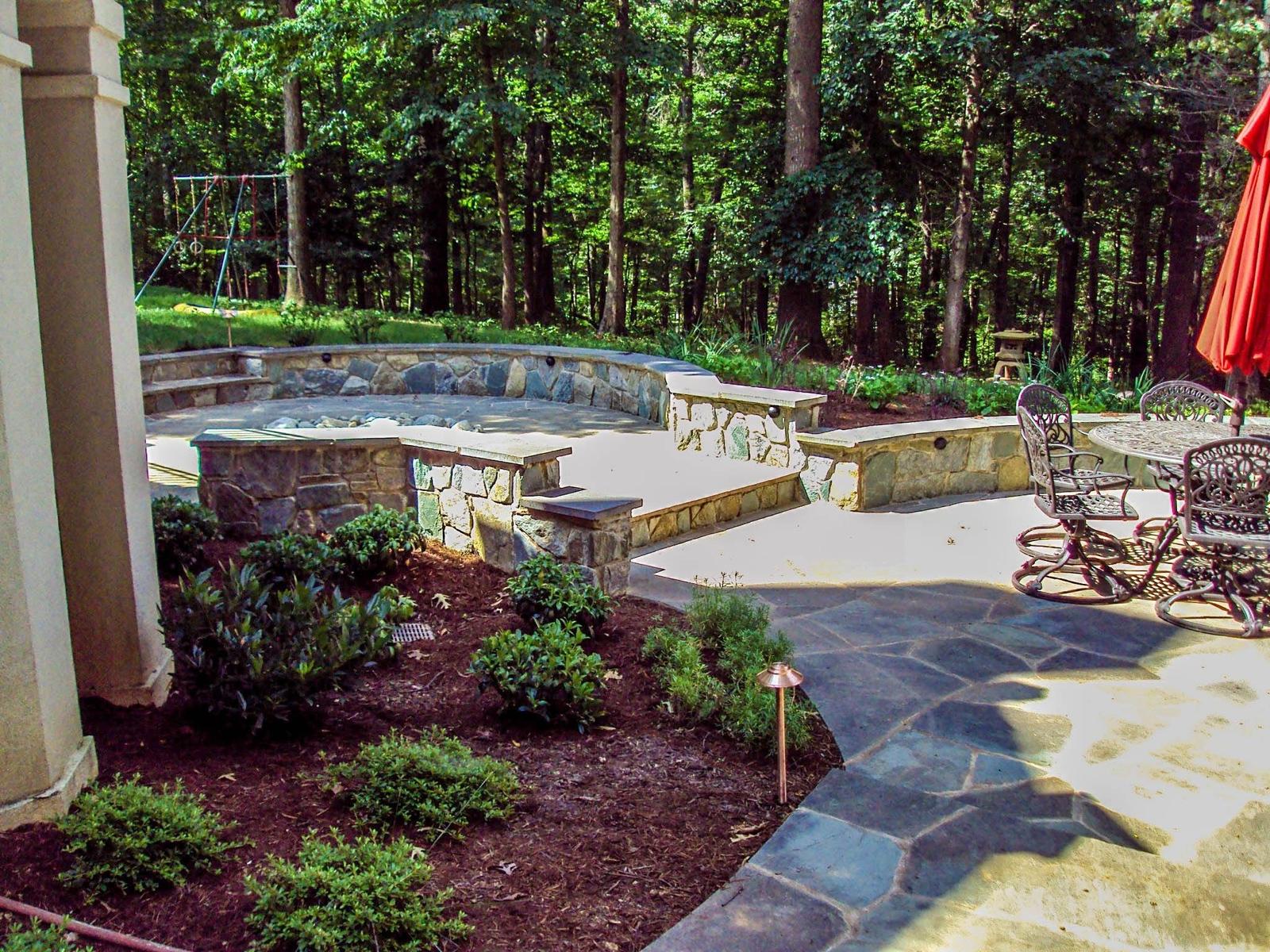 Terraced stone seating walls, steps, and fire pit patio with landscape lighting by Outdoor Solutions