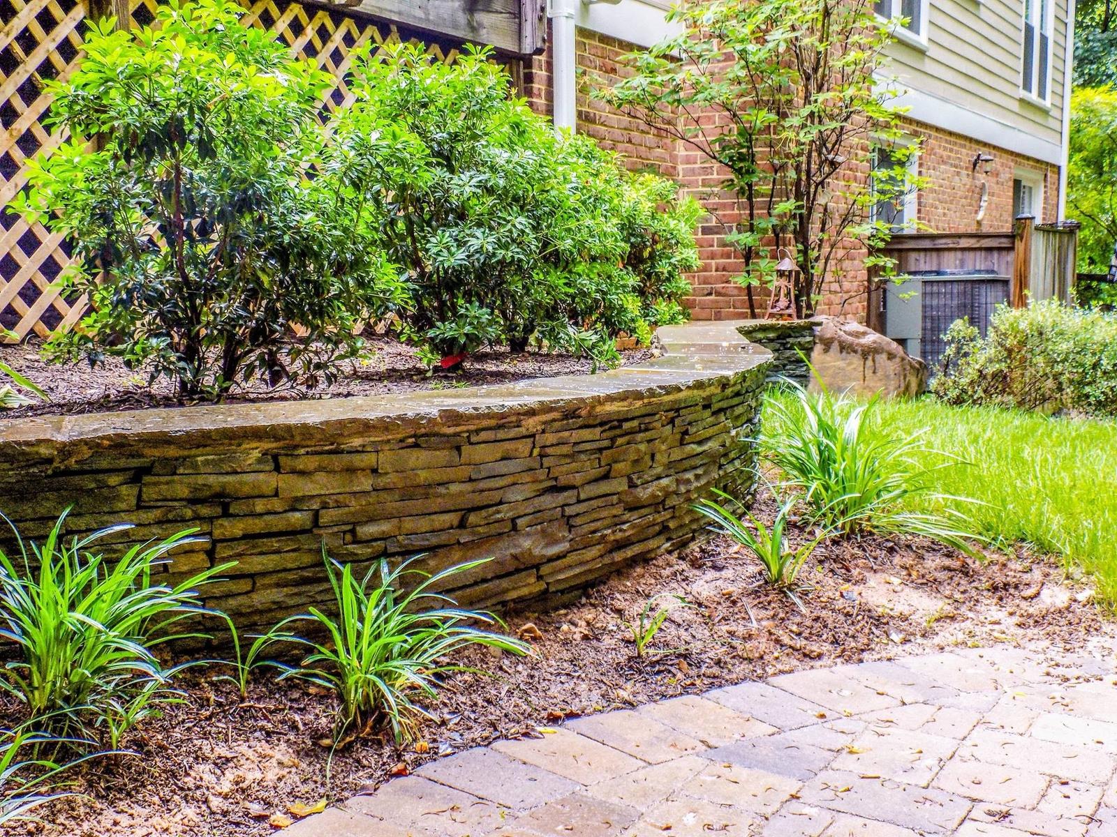 Curved dry-stacked stone retaining wall with flagstone cap and new plantings by Outdoor Solutions